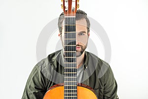 handsome man covering eye with acoustic guitar neck and looking at camera