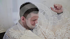 Handsome man crying on a sofa with a wedding dress in his hands.