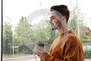 handsome man with cup of coffee near window on rainy day