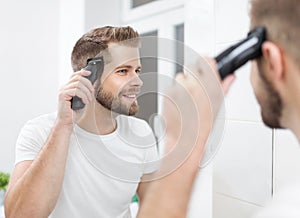 Handsome man cutting his own hair with a clipper