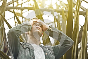 Handsome man in depression. Not shaved hipster in a botanical garden, holding on to his head. Concept: headache and grief