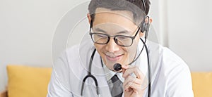 Handsome man doctor speaking microphone with headset to patient at work in home office, online conference.