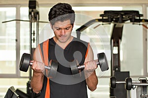 Handsome man doing biceps lifting with dumbbell on bench in a gym