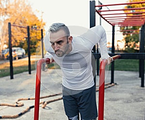 Handsome man doing dips on parallel bars boosting his chest muscles