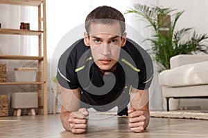 Handsome man doing plank exercise on floor at home