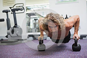 Handsome man doing push ups with kettle bells in gym