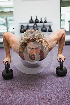 Handsome man doing push ups with kettle bells in gym