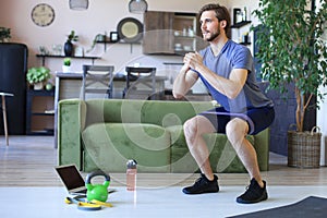 Handsome man doing squats exercise at home during quarantine. Concept of healthy life