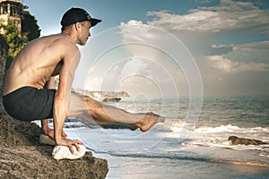 Handsome man doing yoga at cliff with blue sea background