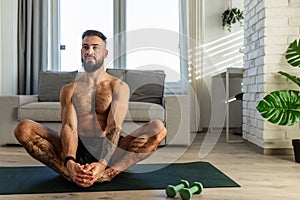 Handsome man doing yoga, stretching, resting after home workout, New Year& x27;s resolutions, exercising as healthy