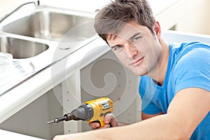 Handsome man with a drill repairing a kitchen sink