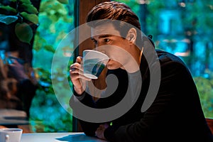 Handsome man drinking tea or coffee on rainy day and looking through the window