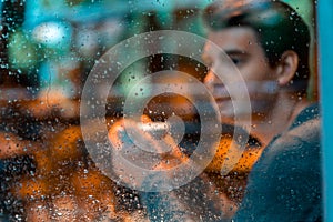 Handsome man drinking tea or coffee on rainy day and looking through the window