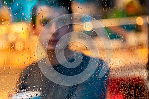 Handsome man drinking tea or coffee on rainy day and looking through the window