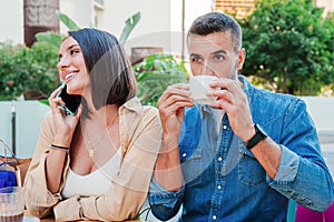 A handsome man drinks and enjoys his coffee cup on a restaurant terrace while his girlsfriend have a phone call