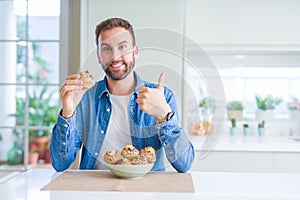 Handsome man eating chocolate chips muffin happy with big smile doing ok sign, thumb up with fingers, excellent sign