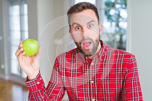 Handsome man eating fresh healthy green apple scared in shock with a surprise face, afraid and excited with fear expression