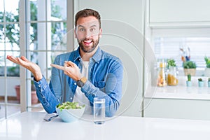 Handsome man eating fresh healthy salad amazed and smiling to the camera while presenting with hand and pointing with finger