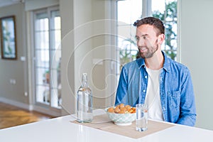 Handsome man eating pasta with meatballs and tomato sauce at home looking away to side with smile on face, natural expression