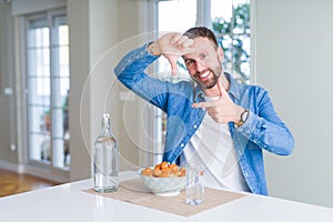 Handsome man eating pasta with meatballs and tomato sauce at home smiling making frame with hands and fingers with happy face