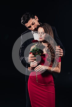 handsome man embracing beautiful woman in red dress holding rose isolated