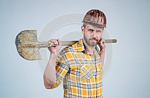 Handsome man expert in construction safety helmet and checkered shirt on building site with shovel, occupation