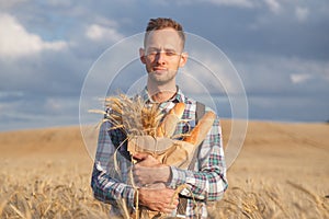 Handsome man farmer or baker with baguettes in rye field