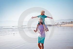 Handsome man father carrying young boy son. Happy dad holding child. Father and son walking on summer beach. Little boy