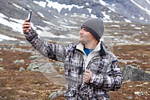 Handsome man finds cell signal in mountains, holding phone with hand up or taking selfie with smartphone camera