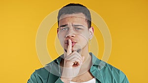 Handsome man with gesture of shh, secret, silence, conspiracy, gossip on yellow