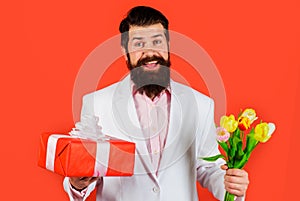 Handsome man with gift and flowers. Businessman with bouquet of tulips and present for birthday. Romantic guy. Valentines Day,