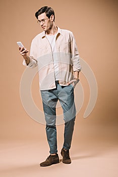 Handsome man in glasses looking at smartphone while standing
