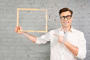 Handsome man in glasses pointing on wooden frame in his hand