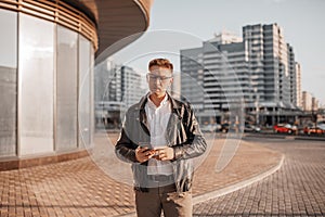 Handsome man with glasses with a smartphone on the street of a big city. Businessman talking on the phone on urban background