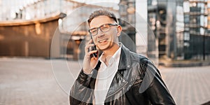 Handsome man with glasses with a smartphone on the street of a big city. Businessman talking on the phone on urban background