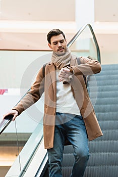 Handsome man in going down on escalator and looking at watch in