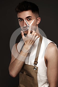 Handsome man hairdresser in a working uniform with scissors in his hands.