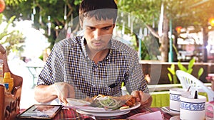 Handsome man has lunch on the tropical island with tablet