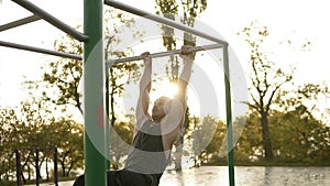 Handsome man having calisthenics training on horizontal bar outdoors. Does gymnastic stunts on the crossbar in the park