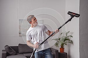 handsome man having fun with vacuum cleaner