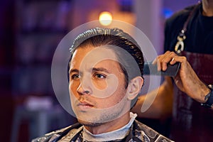 Handsome man is while having his hair cut by hairdresser at the barbershop, close up portrait. Work in the Barber shop