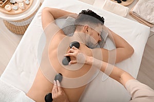 Handsome man having stone massage in spa salon