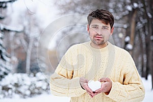 Handsome man with a heart made of snow in his hands