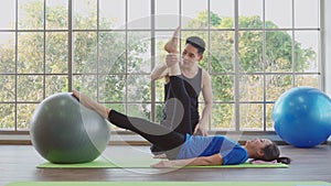 Handsome man helping woman strength training her legs using fitness ball. Togetherness concept