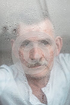 Handsome man in his 50s looking out of window on rainy day