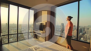 Handsome man in his room in luxury hotel is looking beautiful sunrise. Nice guy lives or freelancing works in hotel. Man