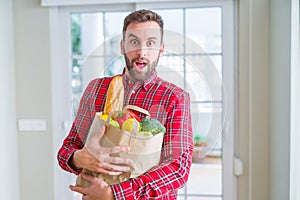 Handsome man holding groceries bag scared in shock with a surprise face, afraid and excited with fear expression