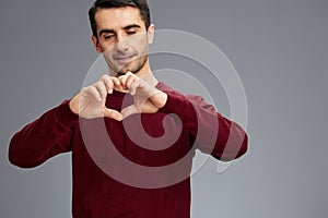 handsome man holding hands in the shape of a heart in a red sweater gesturing with hands posing