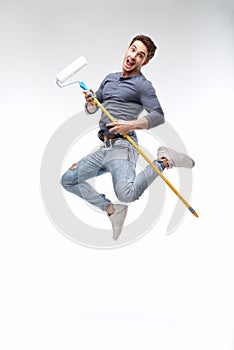 Handsome man holding paint roller and jumping isolated on white