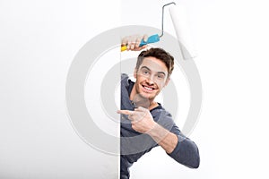 Handsome man holding paint roller and pointing on blank card isolated on white